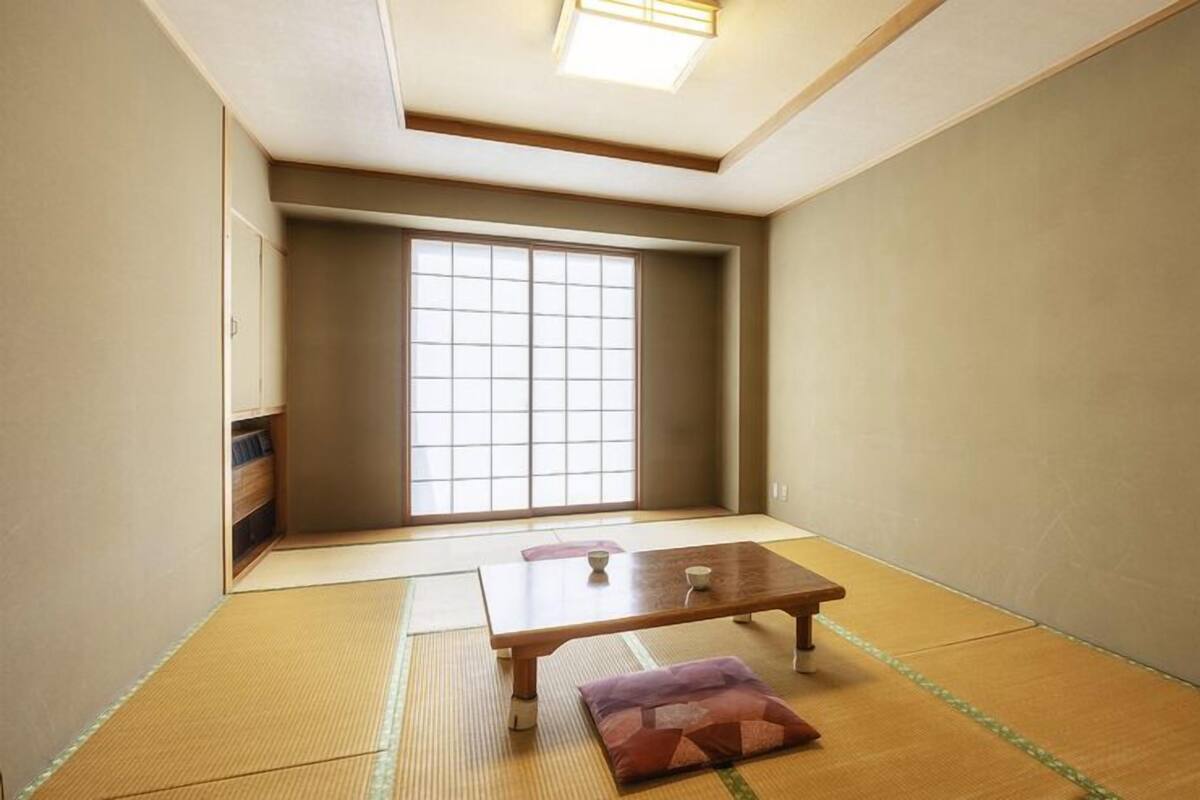 A traditional Japanese room with tatami flooring, a sliding door, and a small table with a cushion.