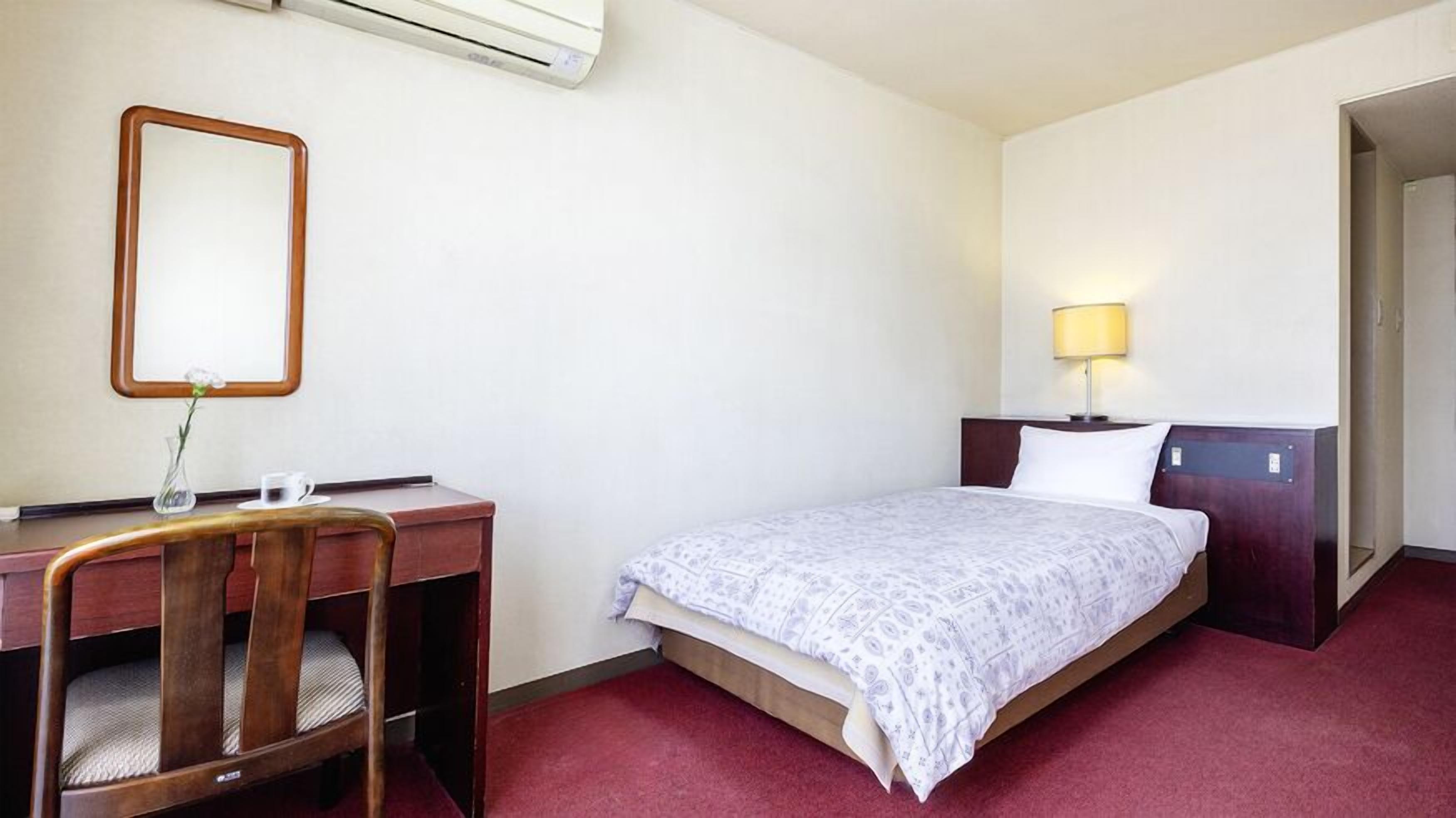Habitación de hotel con cama, escritorio, silla, lámpara y equipo de aire acondicionado.