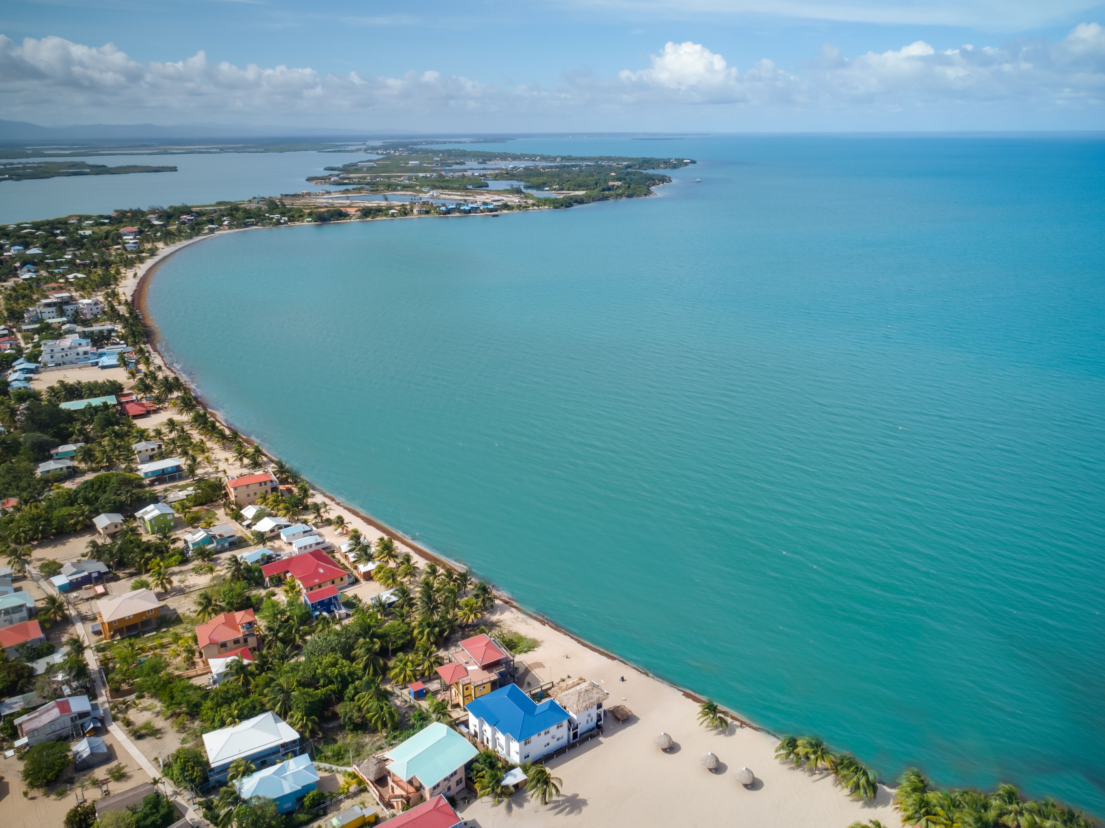 An aerial view of a coastal area with a beach, houses, and clear blue waters.