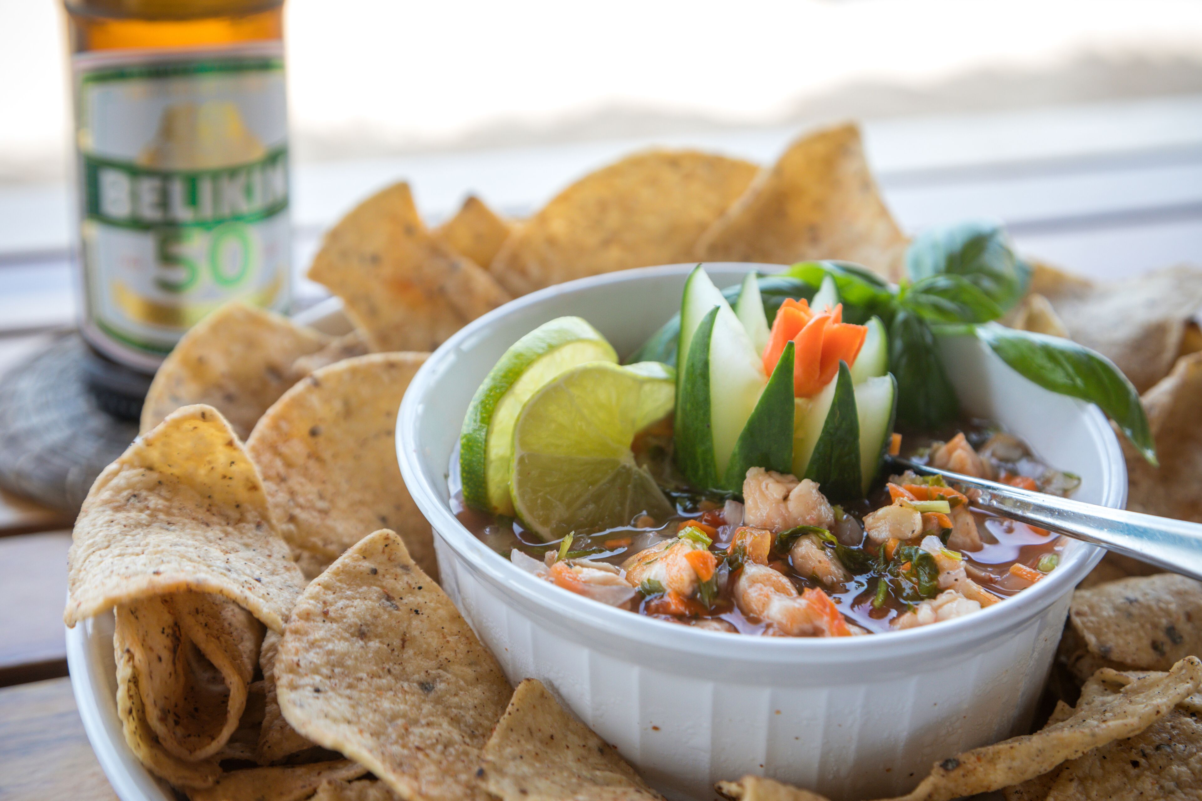 A bowl of soup with vegetables and a spoon, surrounded by tortilla chips.