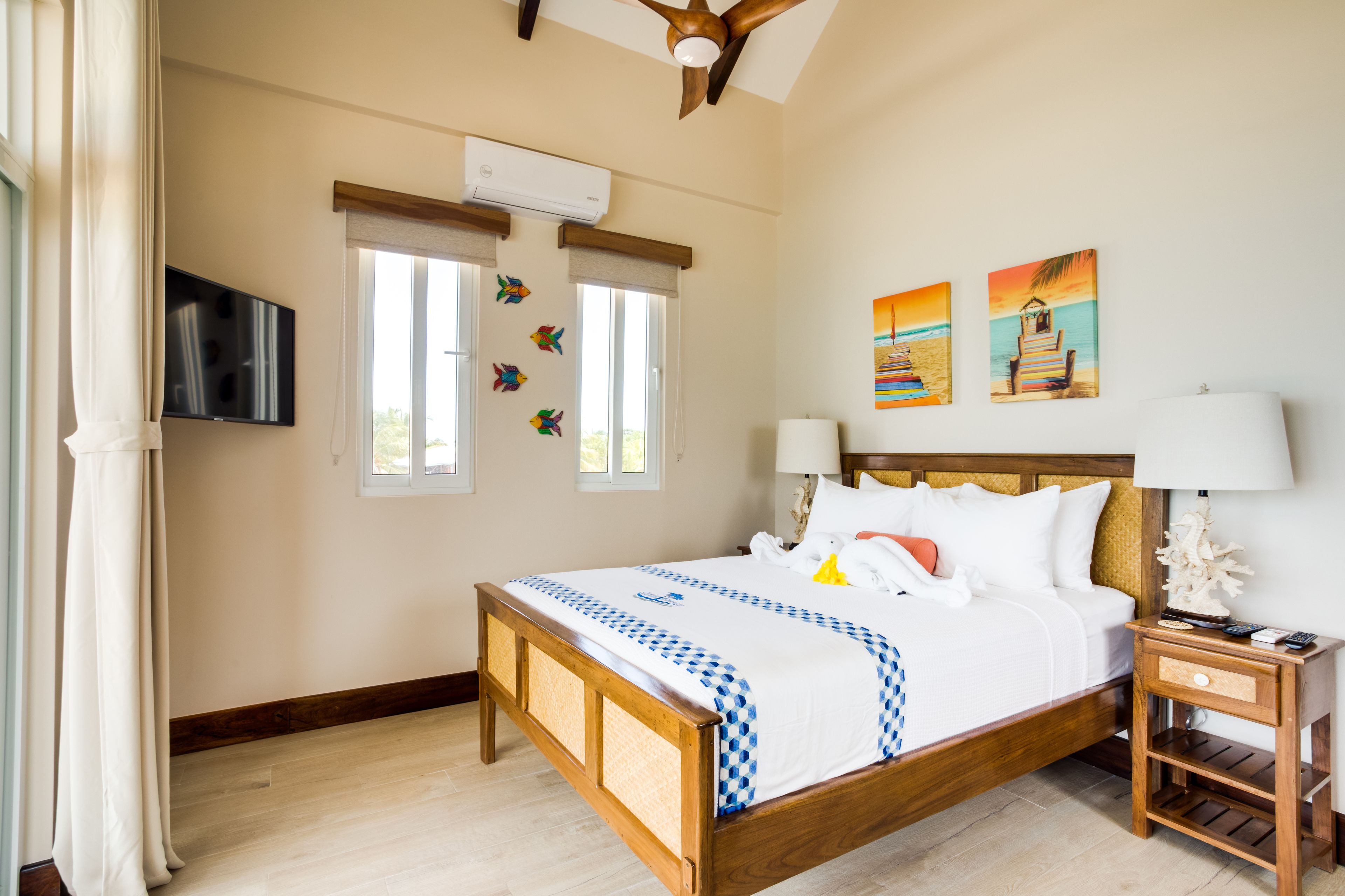 A hotel room with a wooden bed, a nightstand, a TV, and two windows with curtains.
