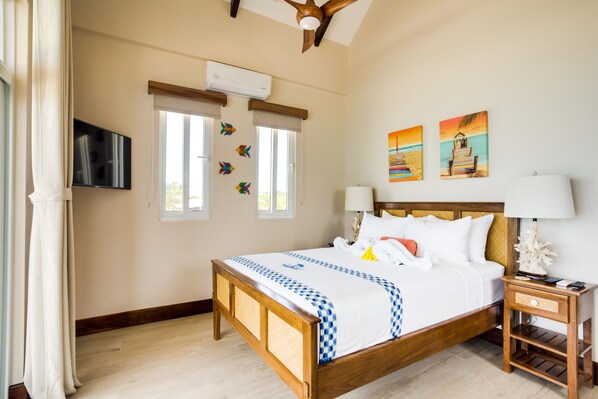 A hotel room with a wooden bed, a nightstand, a TV, and two windows with curtains. - Ocean Breeze (Placencia)