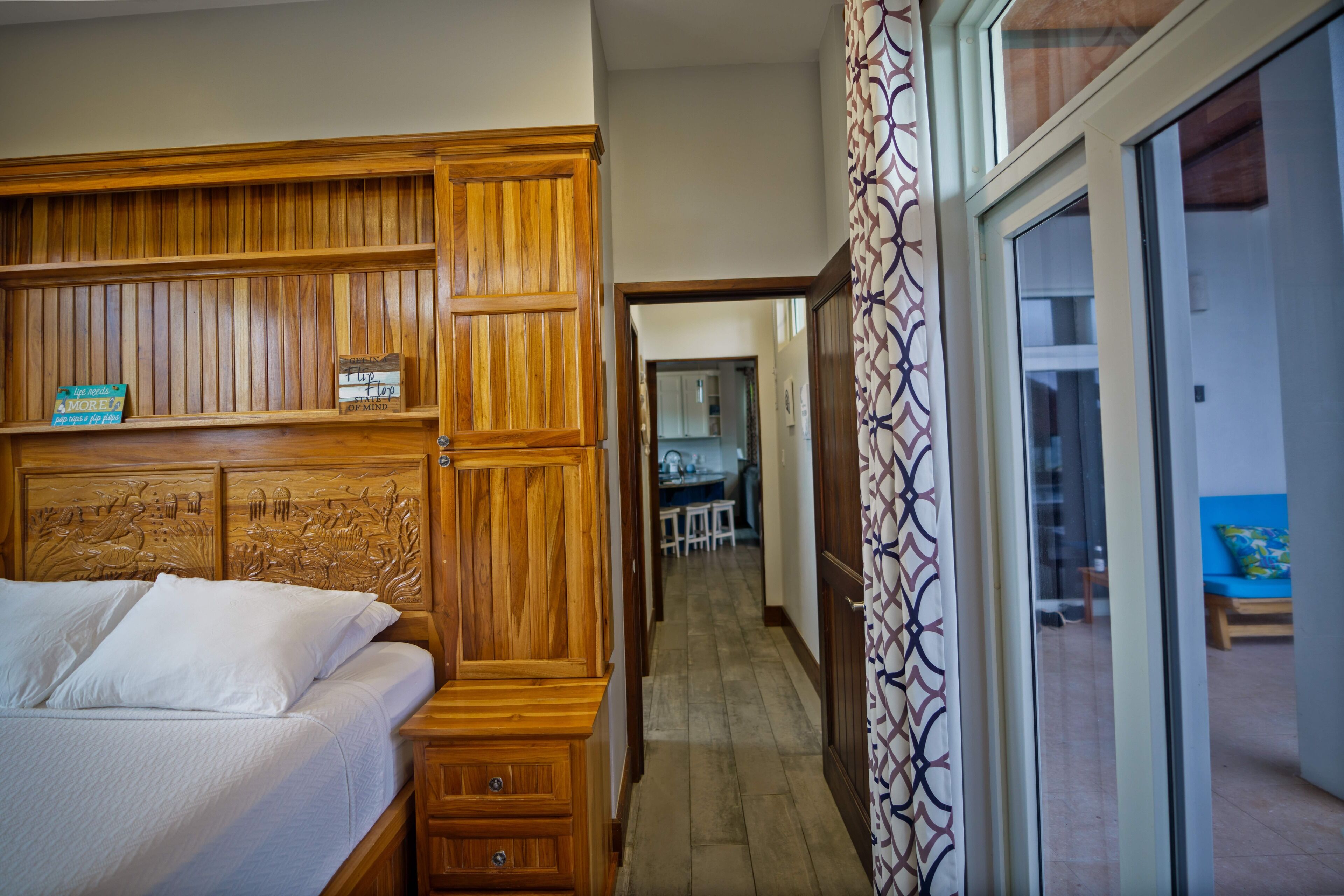 Un dormitorio con cabecera de madera, una cama con ropa de cama blanca y una mesita de noche pequeña con cajones.