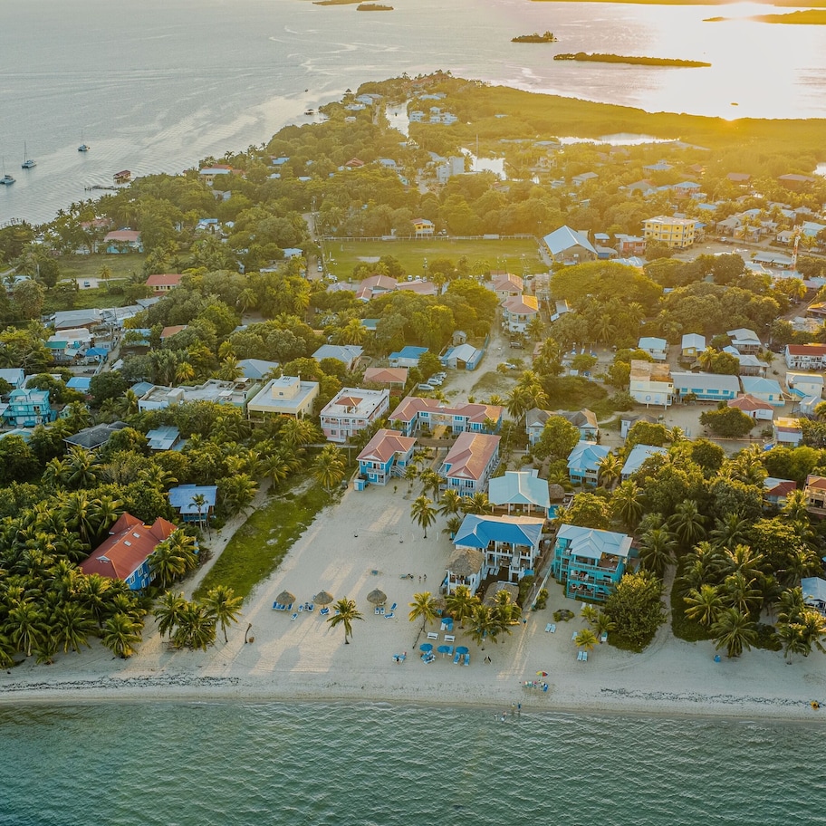 An aerial view of a coastal resort with multiple buildings, a sandy beach, and boats in the water.