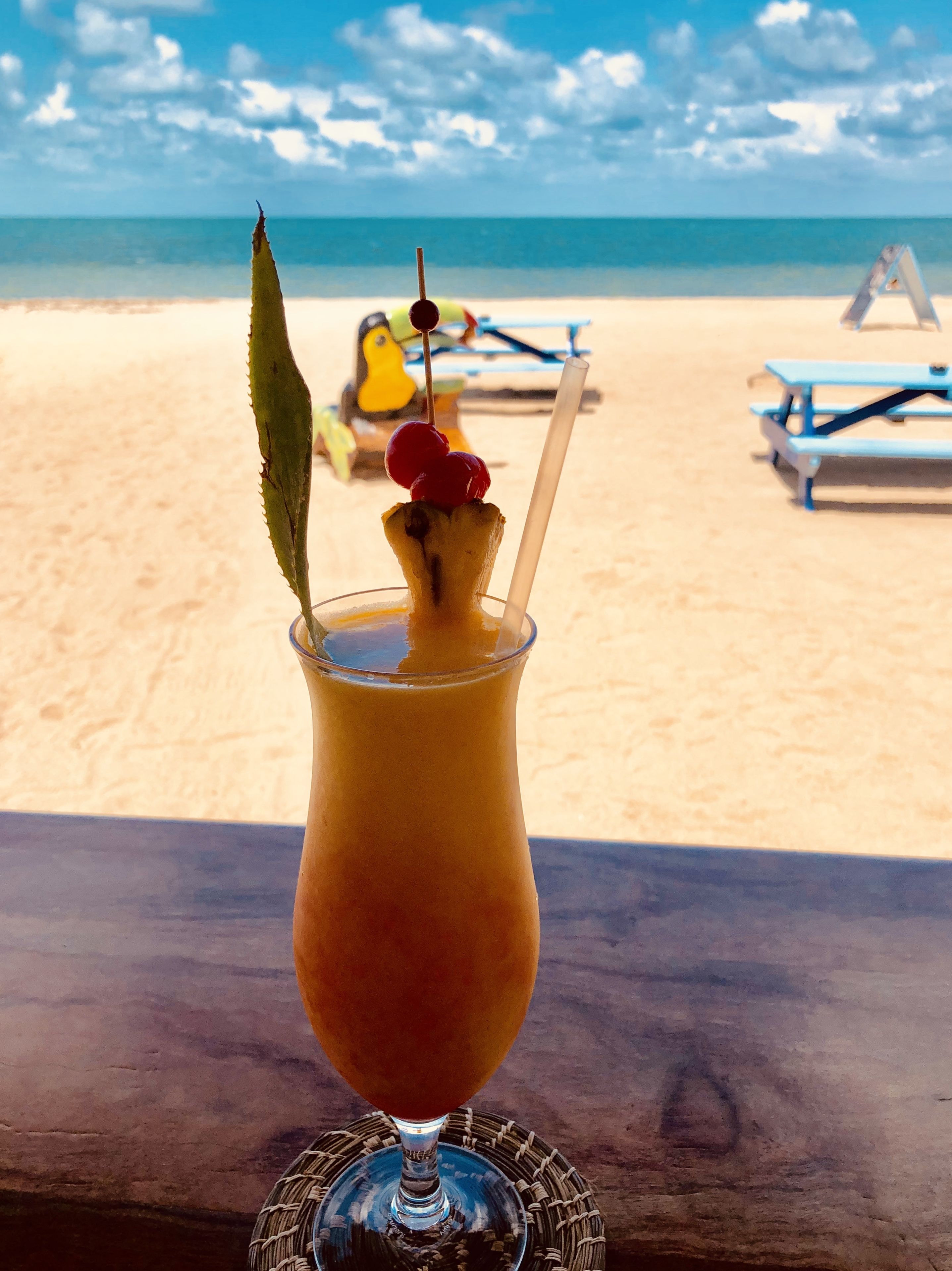 Una bebida tropical en la playa con vista al océano y sillas de playa al fondo.