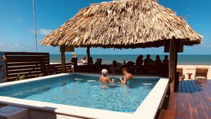 A swimming pool with a thatched roof, wooden deck, and a view of the ocean. - Ocean Breeze (Placencia)