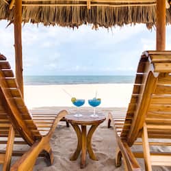 Relax on the beach with a refreshing drink in hand, surrounded by a thatched roof and comfortable seating.