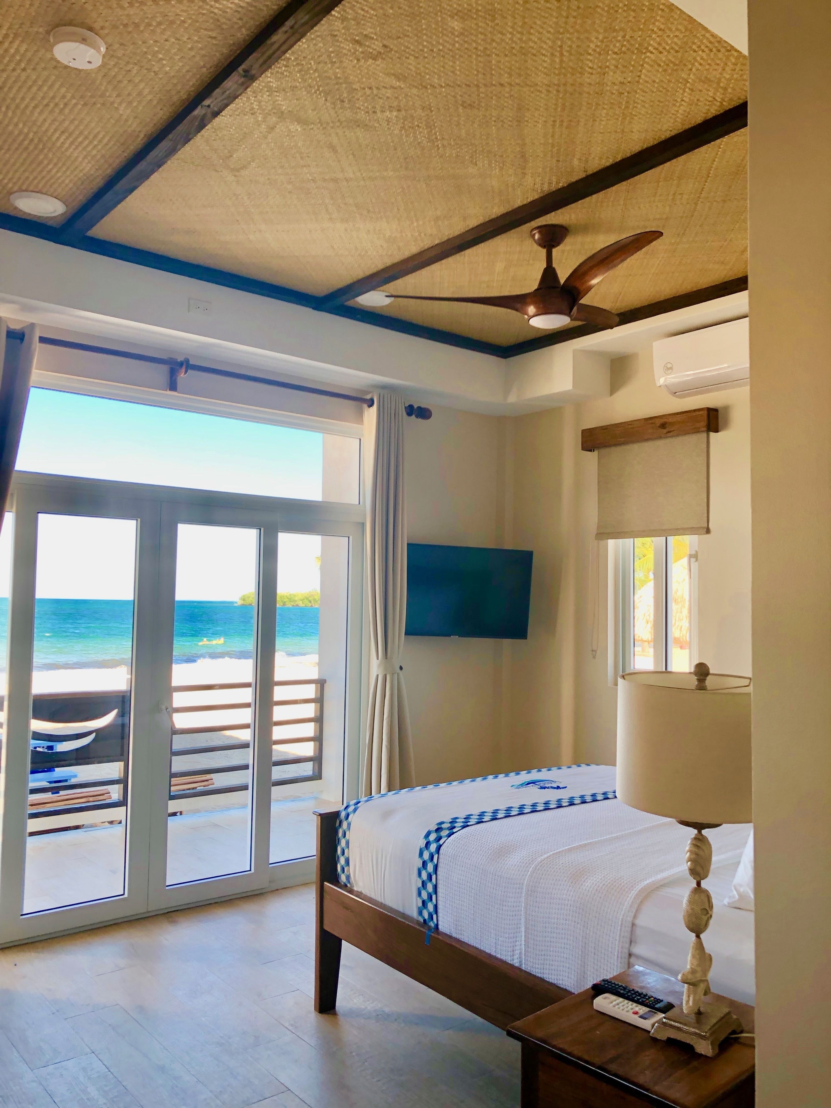 A bedroom with a bed, a ceiling fan, a TV, and a view of the ocean.