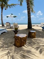 A beach setting with lounge chairs, a table, and a wooden stump.