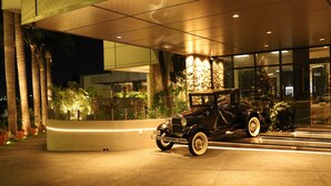 Une voiture noire classique est garée devant un immeuble à la façade en pierre et aux fenêtres en verre.