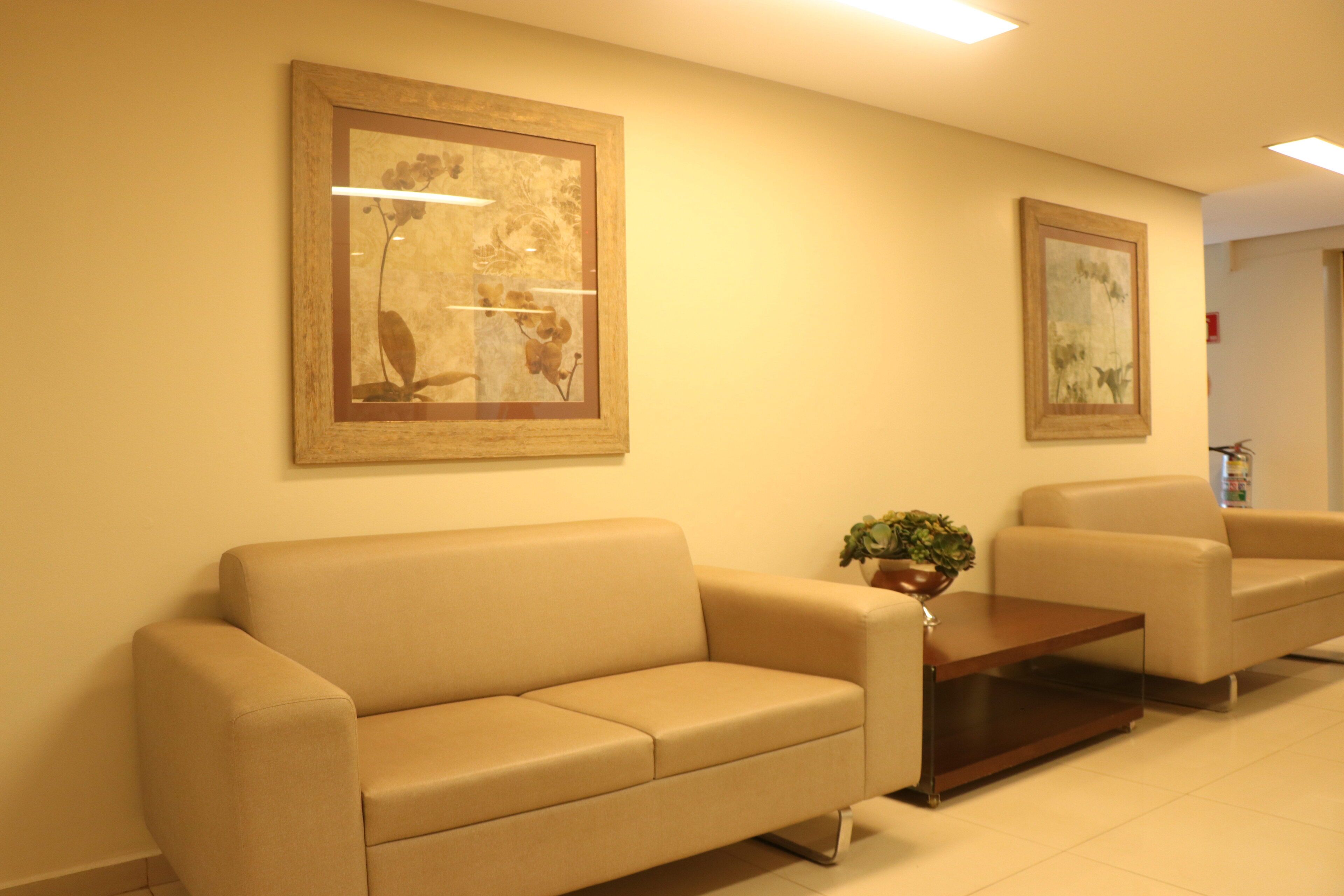 Un área de recepción con dos sofás beige, una mesa de centro de madera y dos cuadros con motivos florales en la pared.