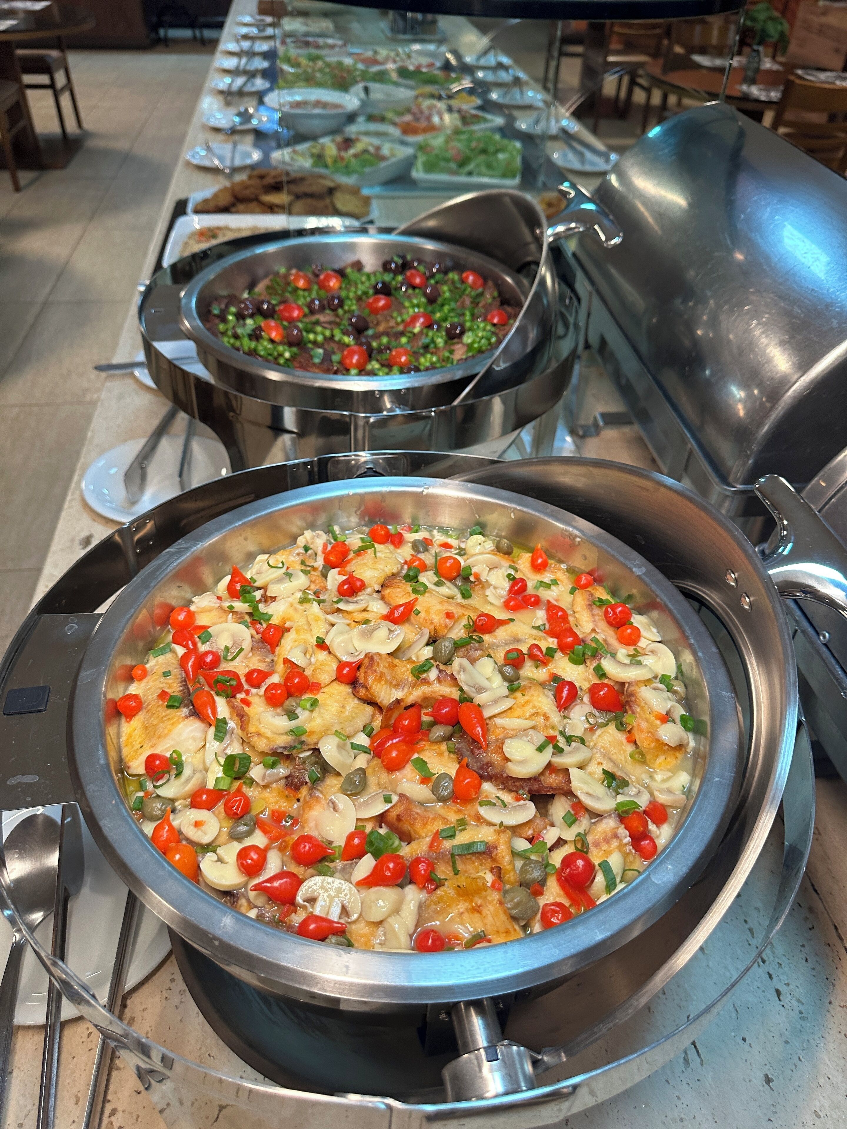 Un bufé con diversos platos, incluyendo una gran olla de mariscos con tomates cherry y cebollas verdes.