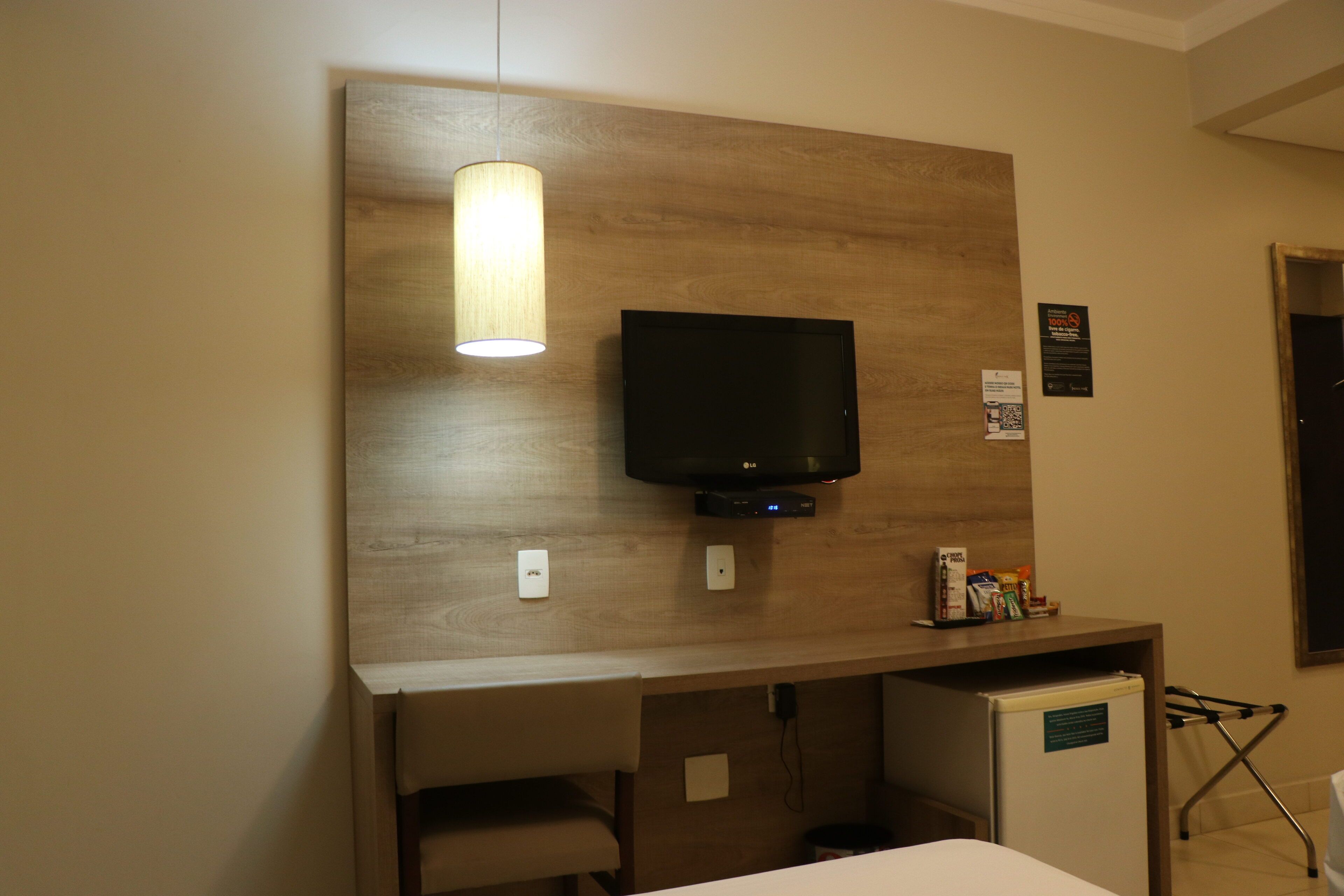 Habitación de hotel con una pared de acento de madera, un televisor de pantalla plana sobre un escritorio, un refrigerador pequeño y una silla.
