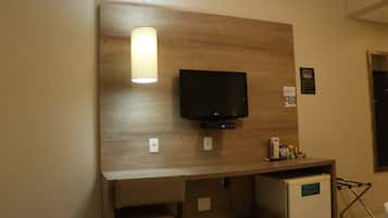 Habitación de hotel con una pared de acento de madera, un televisor de pantalla plana sobre un escritorio, un refrigerador pequeño y una silla.