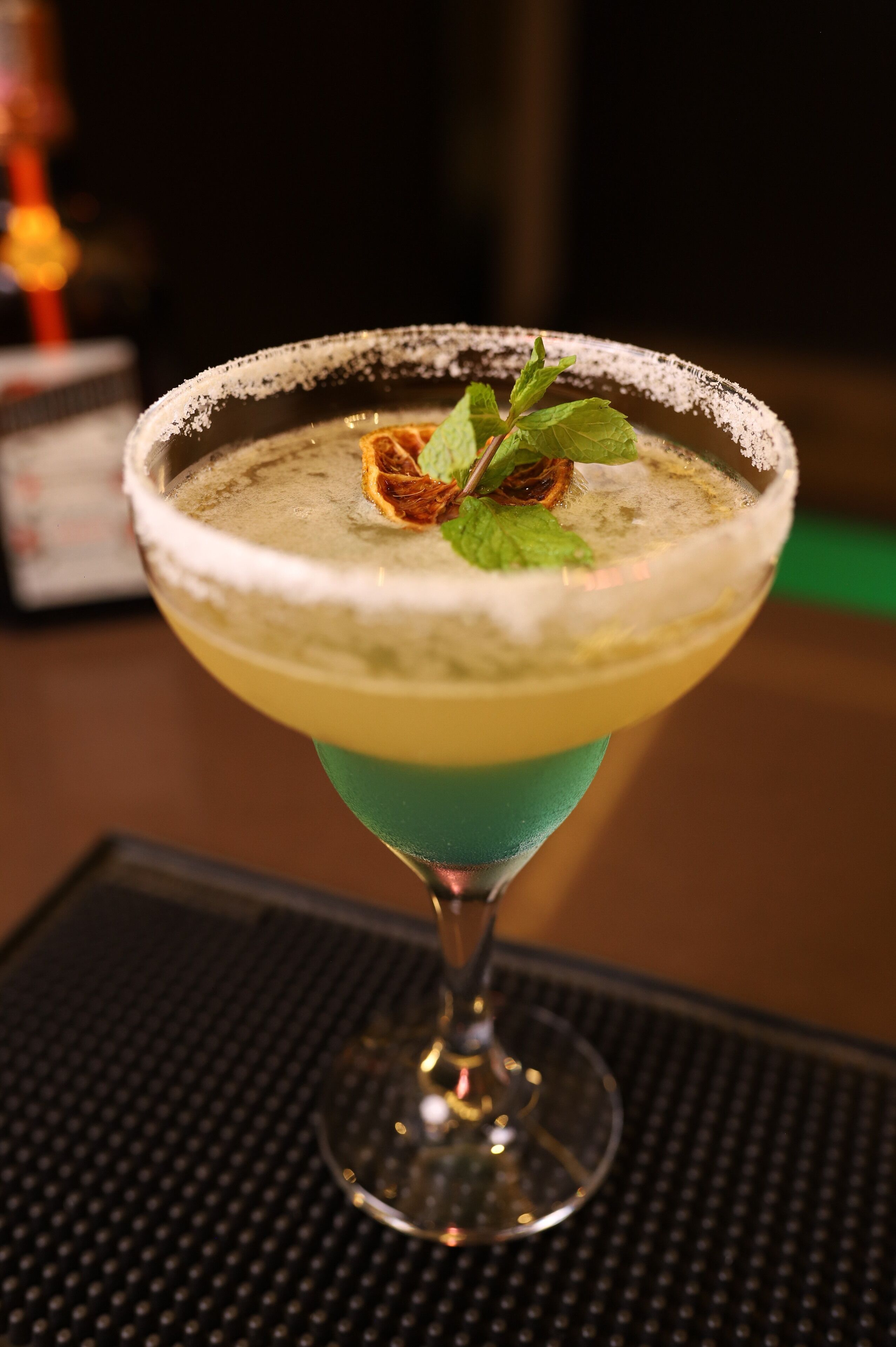 Un còctel en un vas de martini amb vora de sal i decorat amb fulles de menta i una fruita seca.