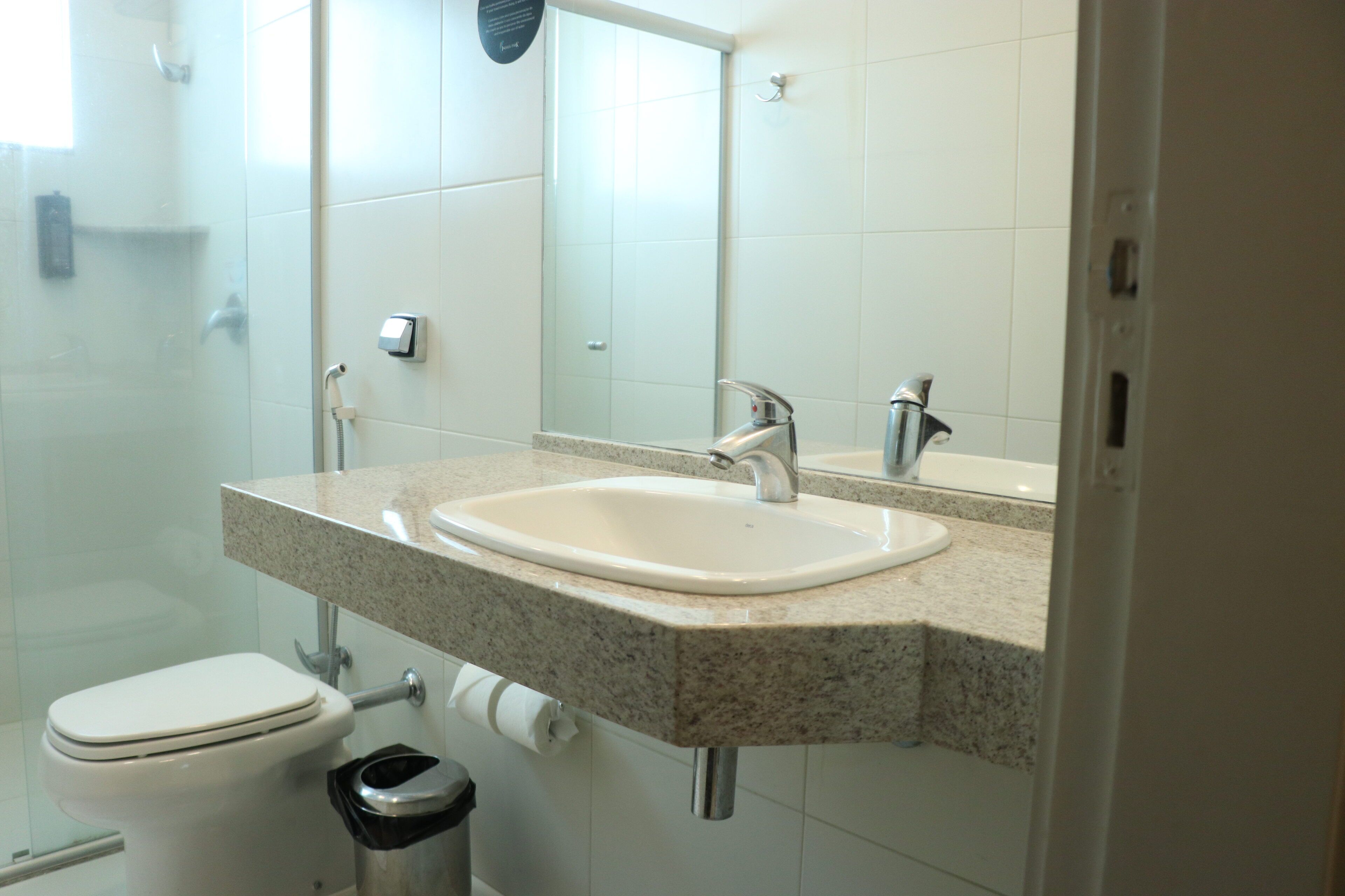 A bathroom with a white sink, a mirror, a toilet, and a trash can.