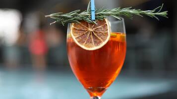 A cocktail glass with a slice of orange and a sprig of rosemary on a bar counter.