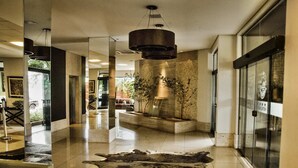 Un hall d’entrée moderne avec un grand tapis en fourrure, un luminaire suspendu et un mur en pierre agrémenté de plantes.