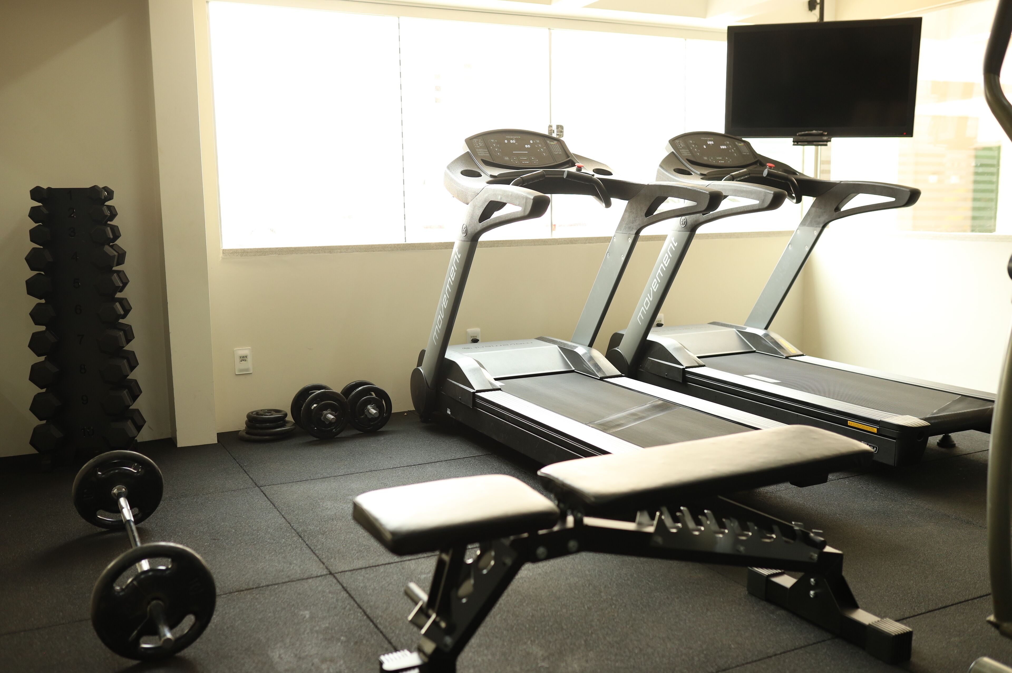 Un gimnasio con cintas de correr, mancuernas y un banco.