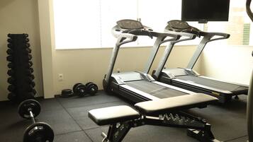 Un gimnasio con cintas de correr, mancuernas y un banco.