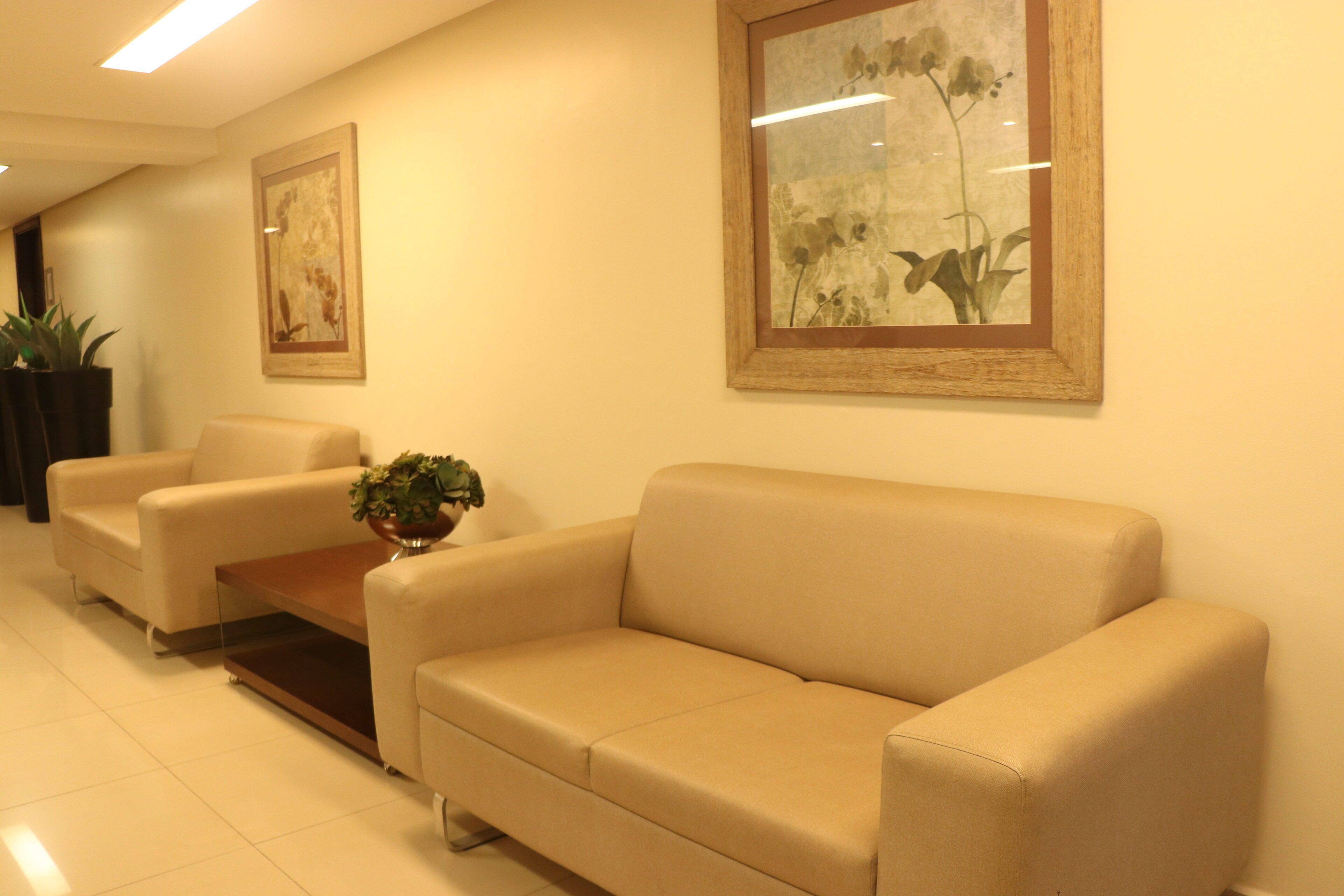 A reception area with a beige sofa, a coffee table, and two framed floral paintings on the wall.