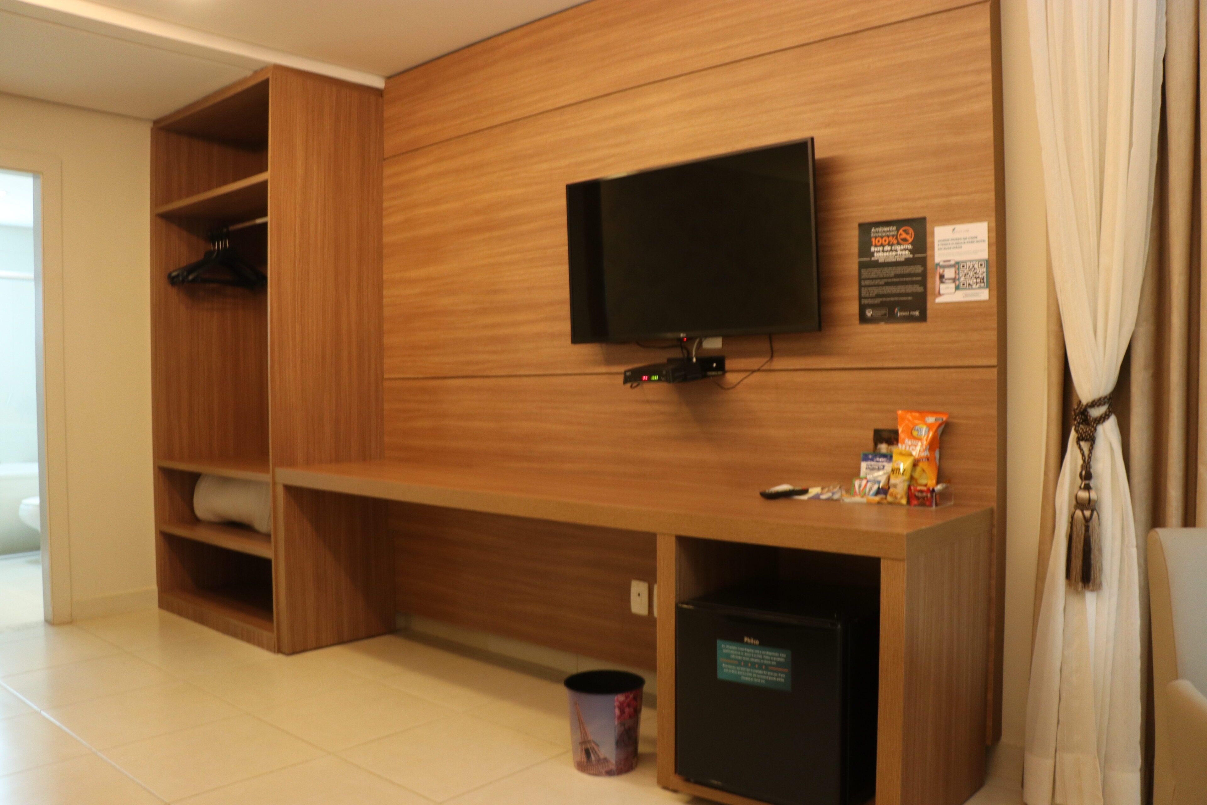 Habitación de hotel con pared de madera, un televisor de pantalla plana sobre un escritorio, un bote de basura y un refrigerador pequeño.
