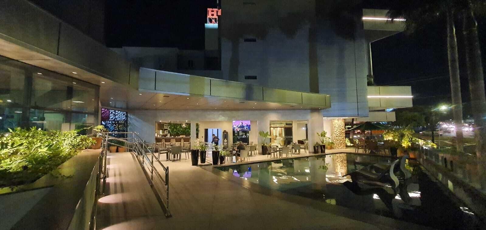 Un moderno vestíbulo de hotel con piscina, asientos al aire libre y una escalera que conduce a pisos superiores.