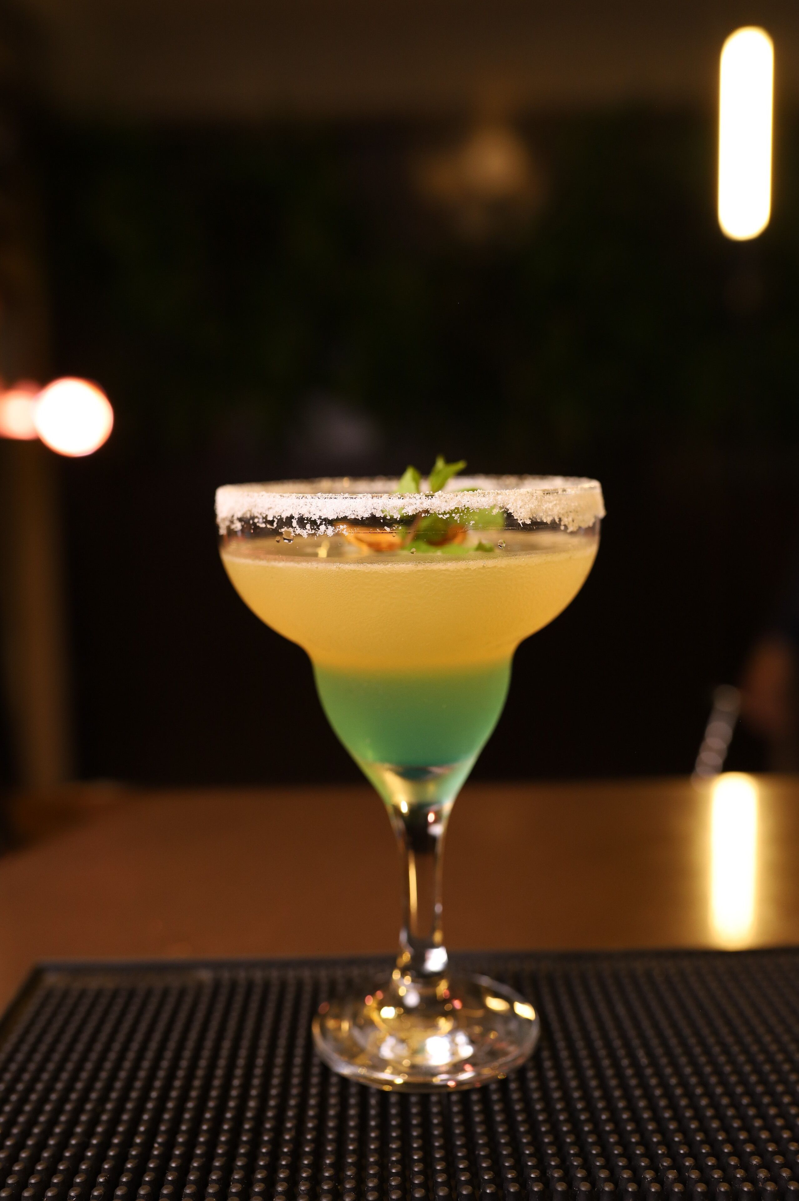 A cocktail in a martini glass with a salted rim on a table.