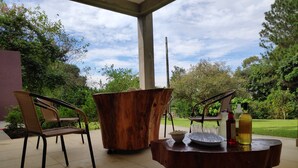 Un espace extérieur abrité, aménagé avec des chaises en osier, une table en bois et un plateau contenant des verres et des bouteilles.