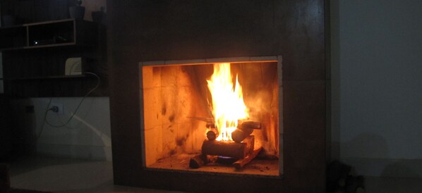 A fireplace with a visible fire burning inside. - Country house in Atibaia - SP (Atibaia)