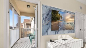 Un balcón con vista a la playa, una consola blanca y un cuadro grande en la pared.
