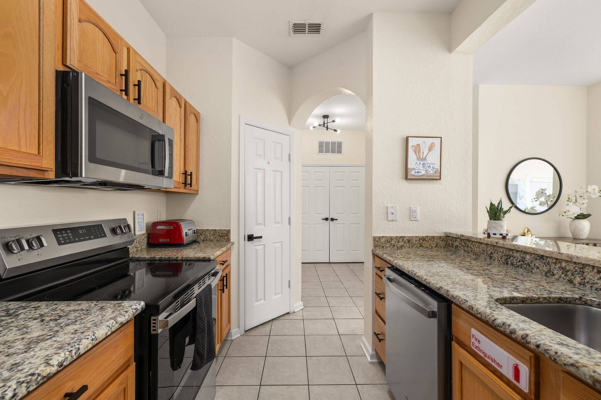 A kitchen with granite countertops, stainless steel appliances, wooden cabinets, a red toaster, and a fire extinguisher sign.