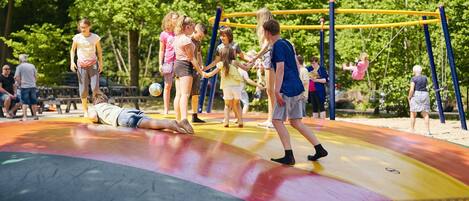 A playground with a colorful surface, a swing set, and a person lying on the ground.