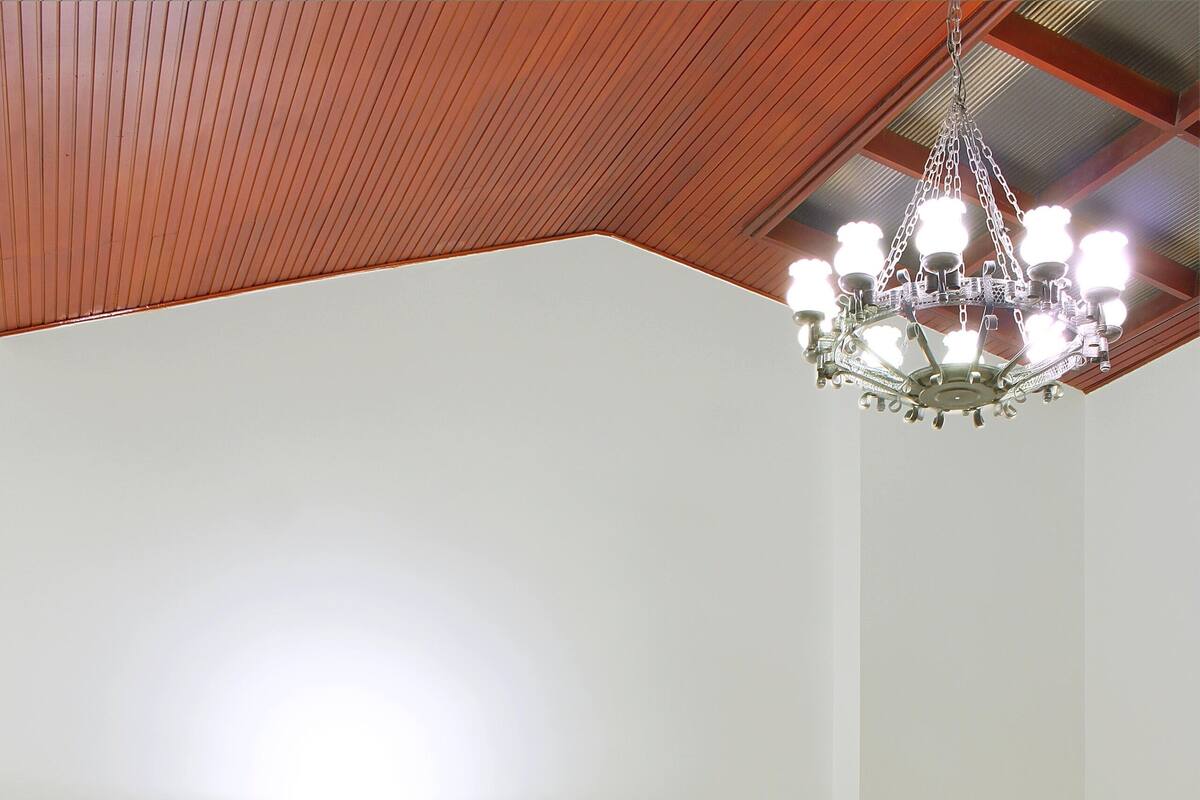 A modern living room with a sofa, a desk with a laptop, a standing lamp, and a chandelier.
