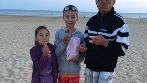 Tre personer står på en sandstrand med havet i bakgrunden.