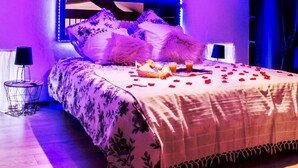 Una cama con una colcha estampada con flores, un almohadar suave y pétalos de rosa esparcidos sobre la cama.