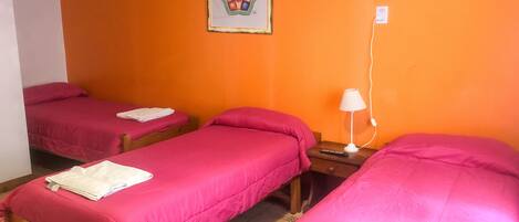 Une chambre avec deux lits, chacun recouvert d’une couvre-lit rose et agrémenté de serviettes blanches. On y trouve une table de chevet avec une lampe et une télécommande.