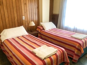 Camera d'albergo con due letti, ciascuno con lenzuola e cuscini a righe. Tra i letti, un comodino con una lampada.