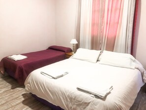 Camera d'albergo con due letti, uno con copriletto bianco e l'altro con copriletto color borgogna. Tra i letti c'è un comodino con una lampada.