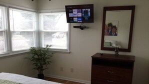 A hotel room with a bed, a TV mounted on the wall, a dresser, and a window with blinds.
