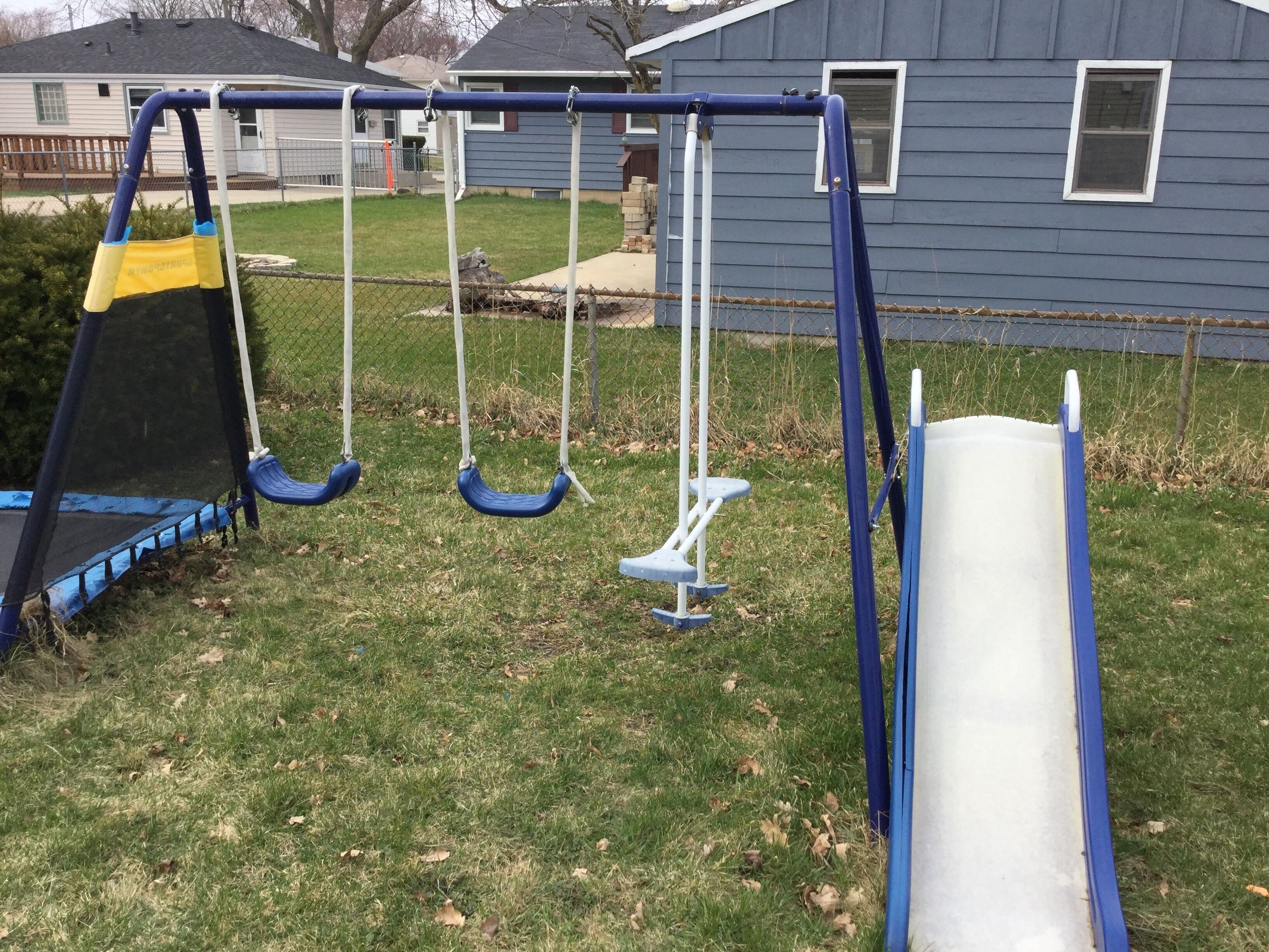A playground with swings and a slide, set against a house and lawn.