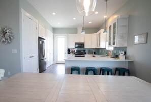 A modern kitchen with white cabinets, a stainless steel refrigerator, a microwave, and teal stools at the island.
