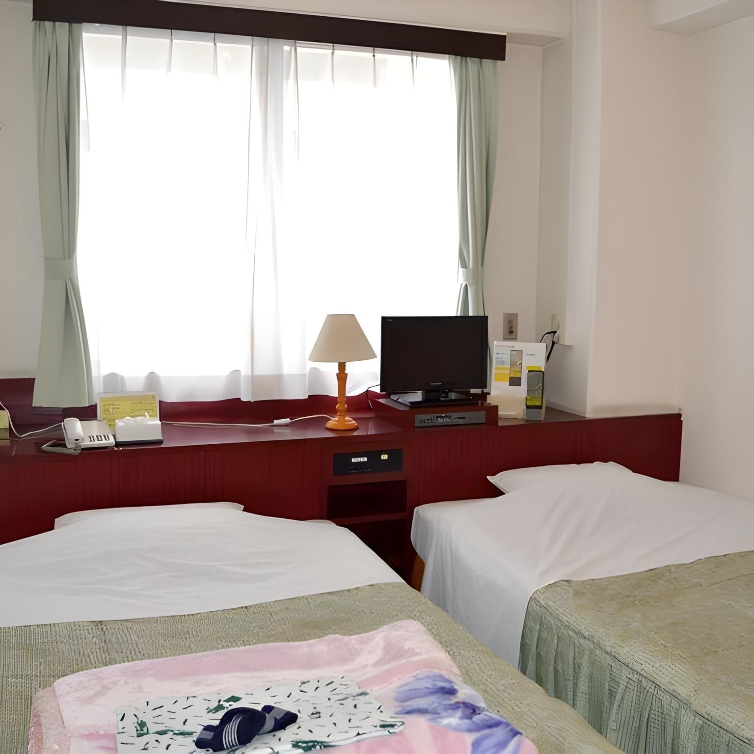 A hotel room with two beds, a desk with a lamp, a television, and a window with curtains.