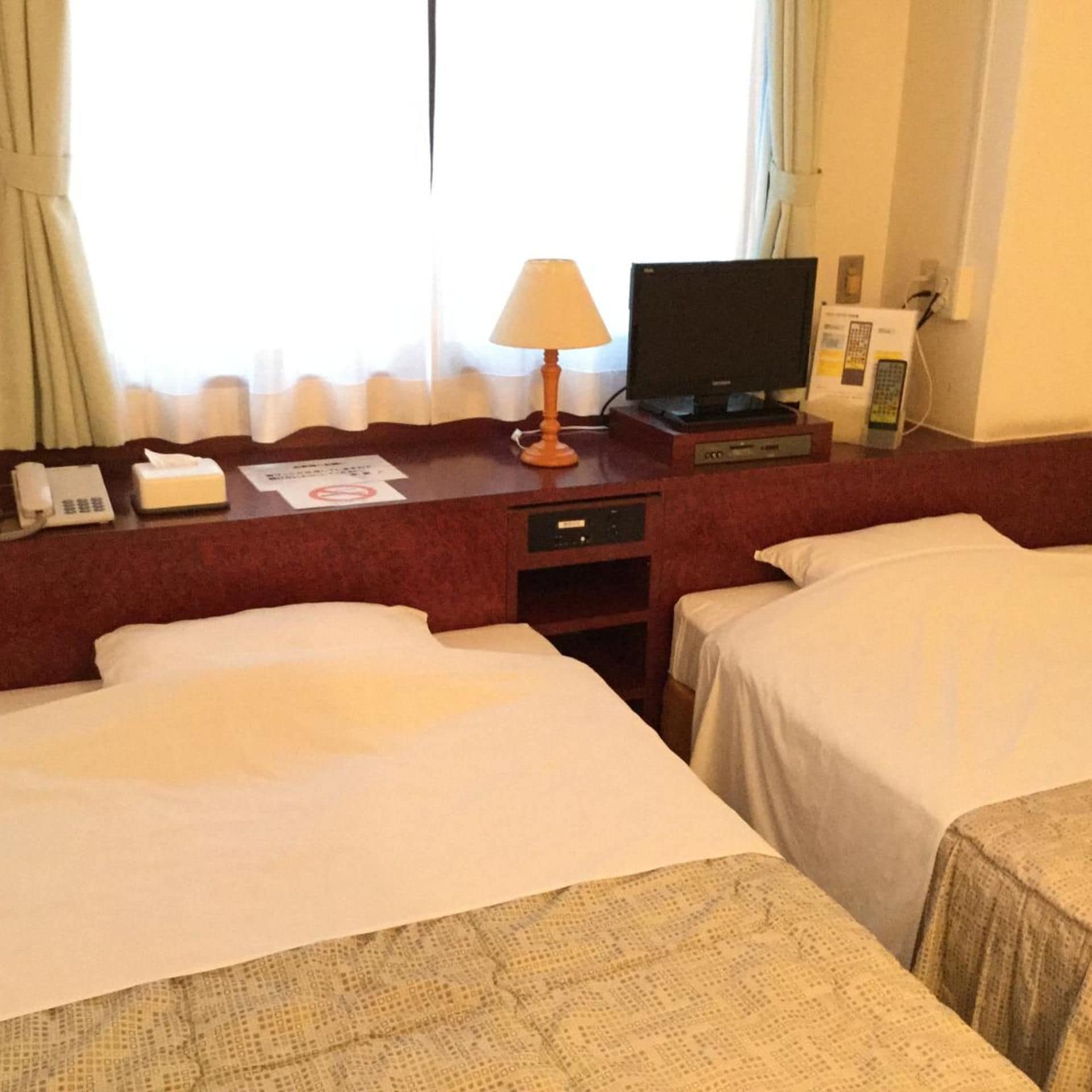 A hotel room with two beds, a desk with a lamp, a television, and a telephone.