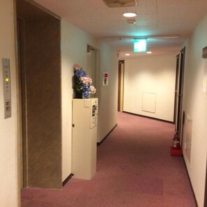 A hallway with a carpeted floor, a fire extinguisher on the right, and a door at the end. - Kisyaba Hotel (Kagoshima)