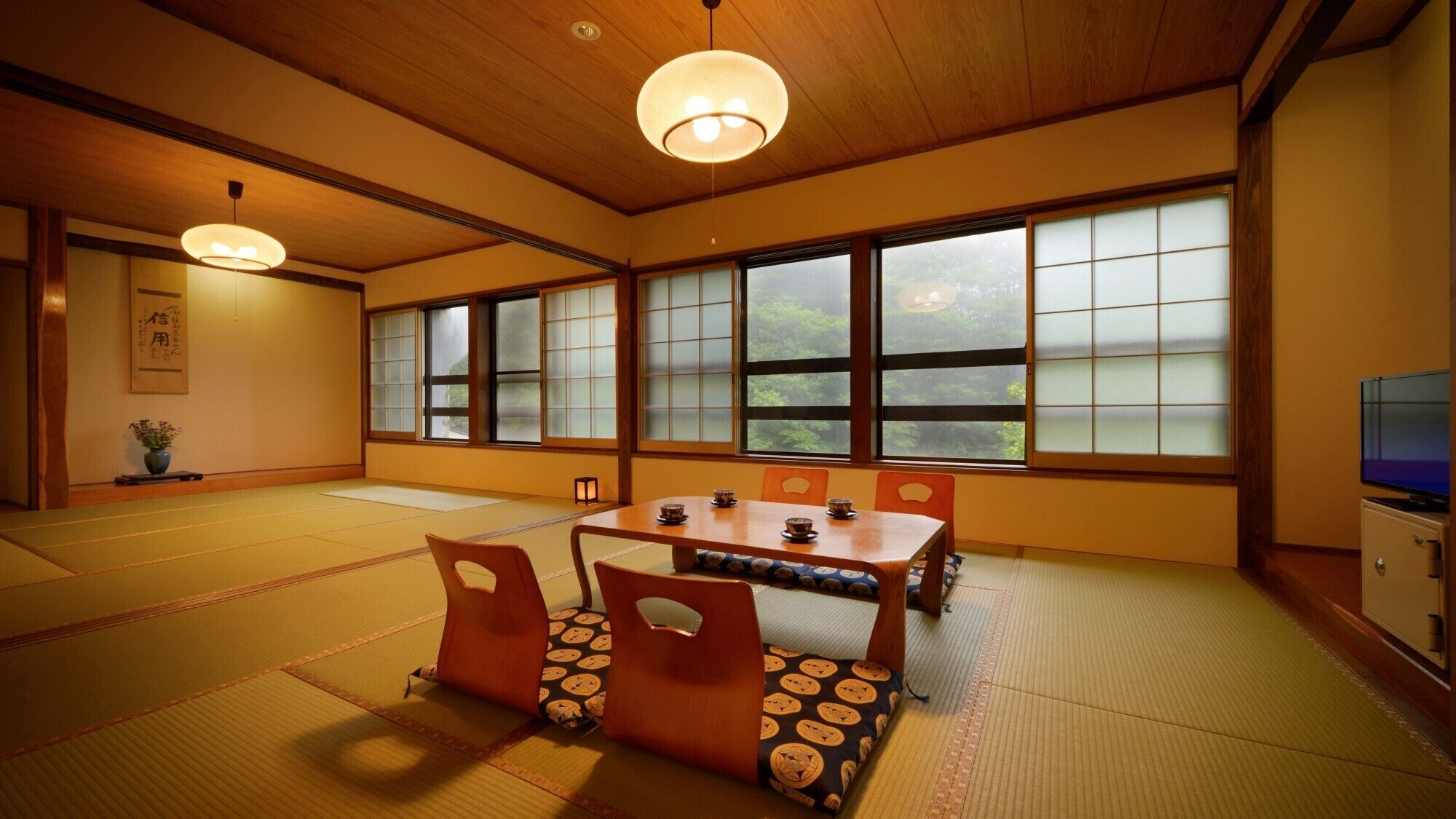 A traditional Japanese room with tatami flooring, a low table with cushions, sliding shoji doors, and a television.