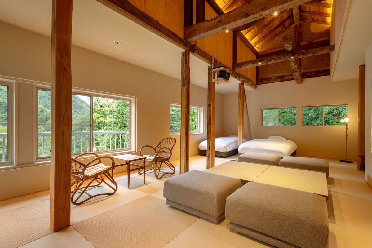 Una habitación amplia con ventanas grandes, una cama, un sofá y una pequeña mesa con sillas.
