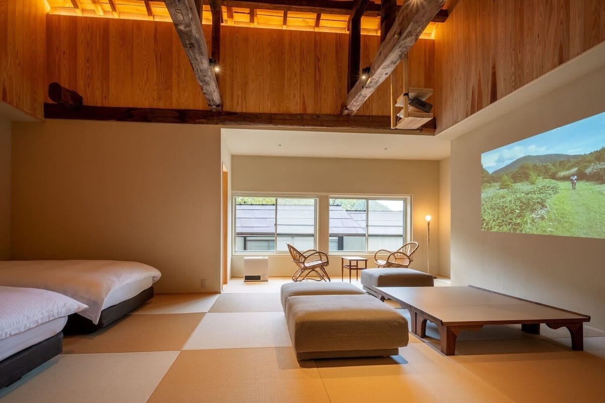 Un dormitorio con una cama, un sofá, una mesa y una pantalla proyectando un paisaje.