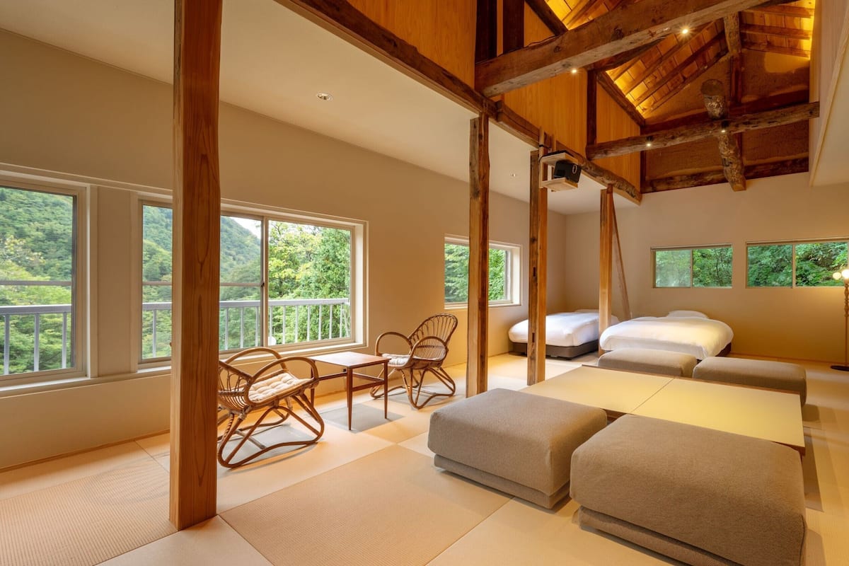 Una habitación con cama, sofá, mesa y sillas, con ventanas amplias y vigas de madera.