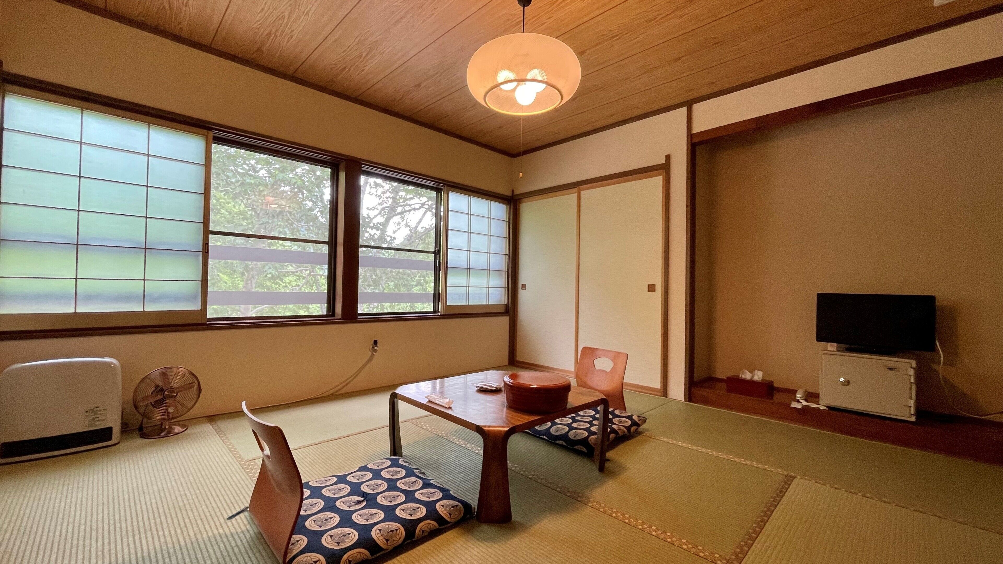 Una habitación japonesa tradicional con suelo de tatami, una mesa baja, un sofá, un abanico y un televisor.